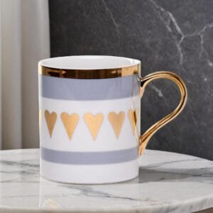 Ceramic mug adorned with golden hearts and a golden handle on a marble table.